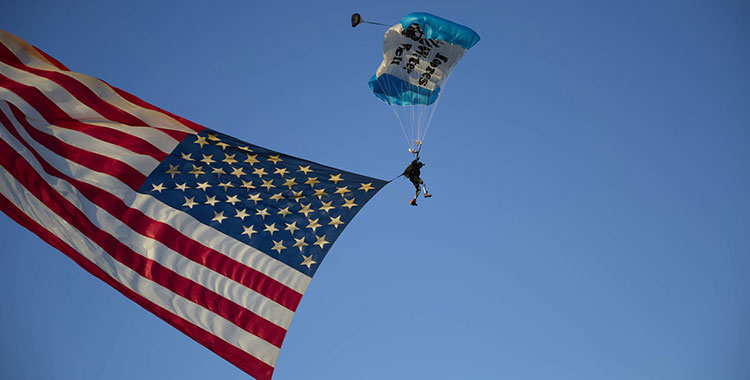 Un veterano que lleva un paracaídas presenta la bandera estadounidense que cae del cielo.